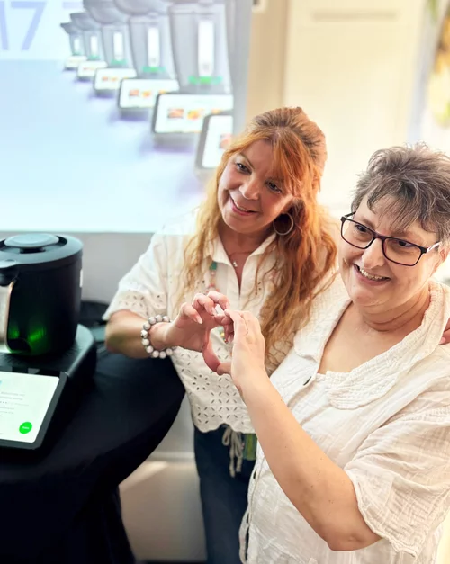 Vorwerk: Foto: Zwei Frauen in Arbeitskleidung wie sie in Pflegeeinrichtungen üblich ist, stehen in einer modernen Küche und zeigen Daumen hoch. Neben ihnen steht ein Thermomix® TM6, worüber sie sich offensichtlich freuen.
