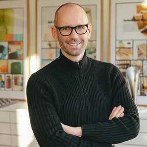Vorwerk: Foto: Das Foto zeigt einen Oberkörper-Ausschnitt von Jan Delfs, Vorwerk Chefdesigner, mit vor dem Bauch verschränkten Armen, der in die Kamera lächelt.