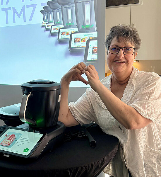 Vorwerk: Foto: Eine ältere Frau formt ein Herz mit ihren Händen. Neben ihr ist ein TM7 zu sehen.