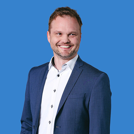 Vorwerk: Foto: Ein Mann in weißem Hemd und blauem Jackett lächelt in die Kamera.