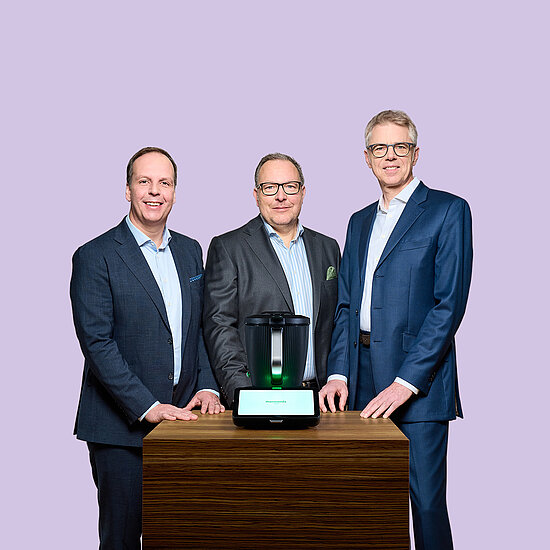Vorwerk: Foto: Dieses Foto zeigt den Vorstand von Vorwerk: links Hauke Pausch, in der Mitte Dr. Thomas Stoffmehl, Sprecher des Vorstands, und rechts Dr. Thomas Rodemann. Vor ihnen steht auf einem Holztisch der Thermomix TM7.