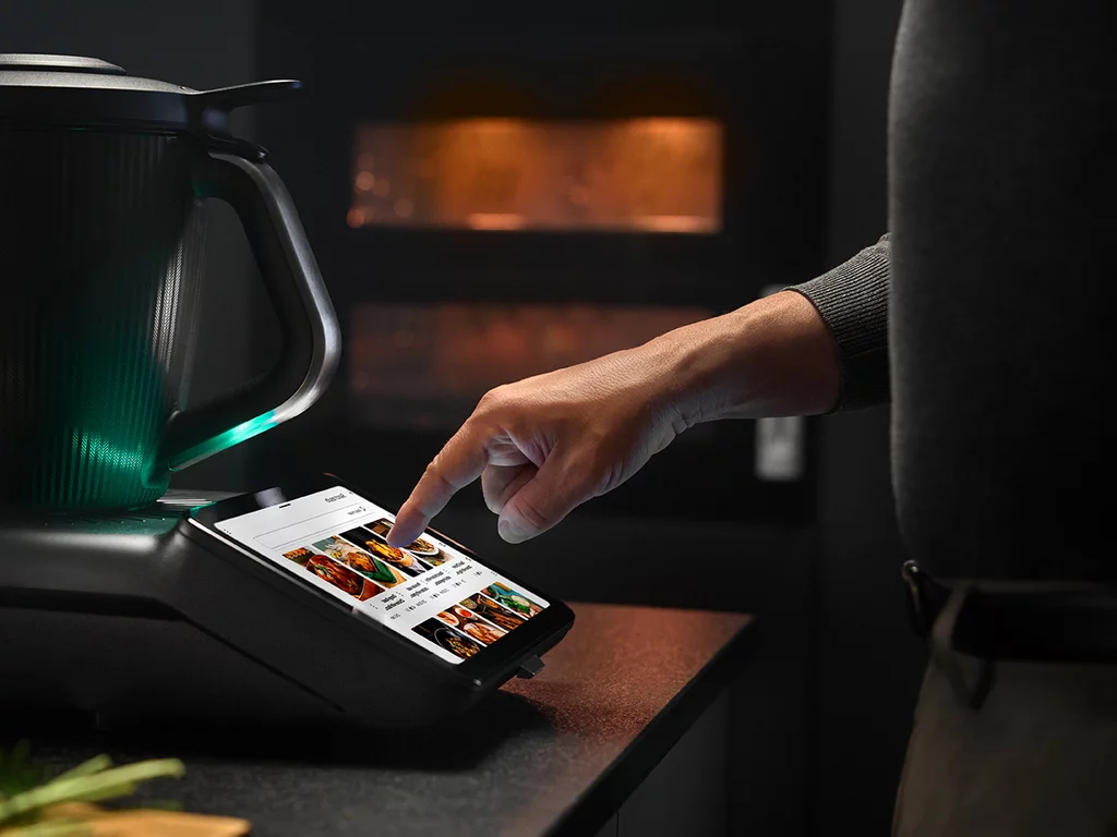 Vorwerk: Foto: Das Bild zeigt den neuen schwarzen Thermomix® TM7, der grün leuchtet, von der Seite.